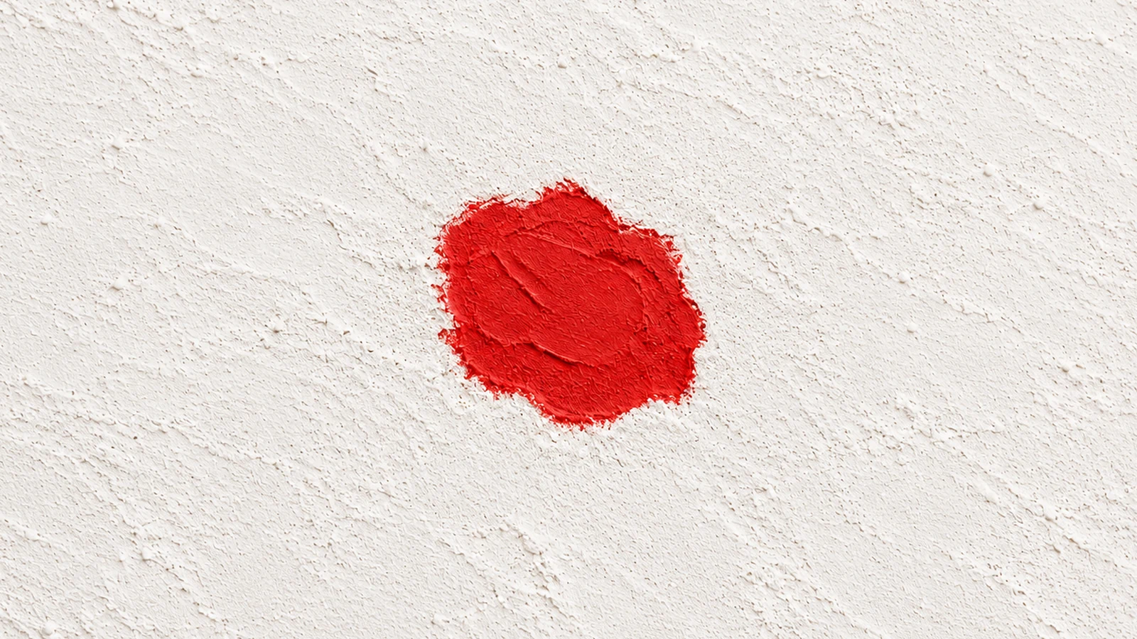 A localized matte red filler patch with shallow trowel marks sits within a broad continuous off-white plaster surface.