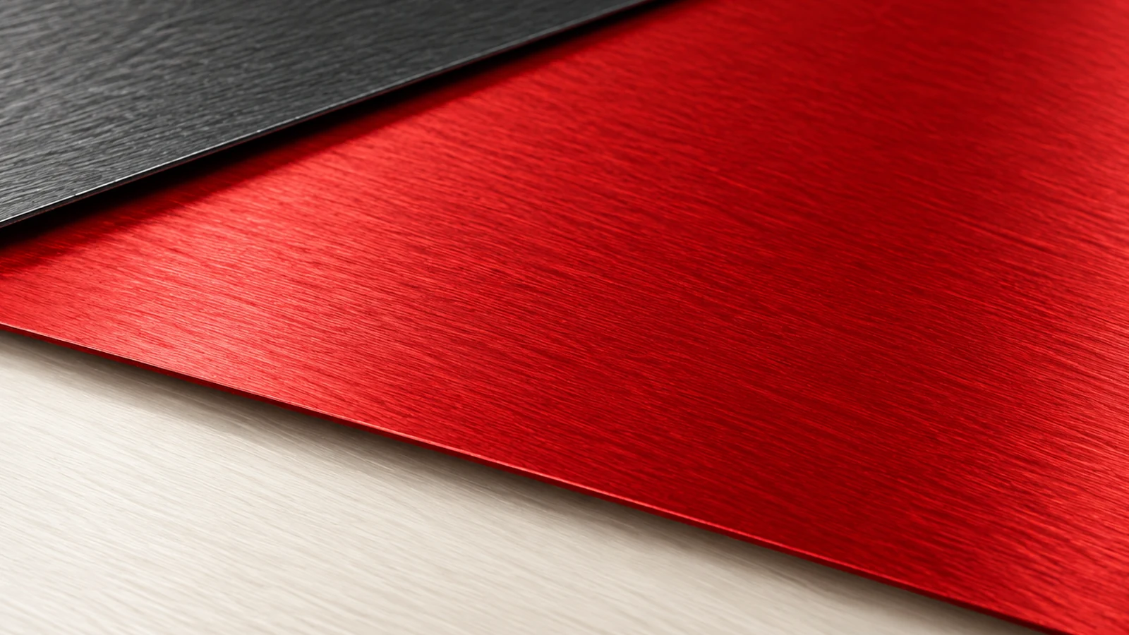 A broad red brushed-metal sheet is exposed between an overlapping charcoal upper sheet and an off-white lower surface.