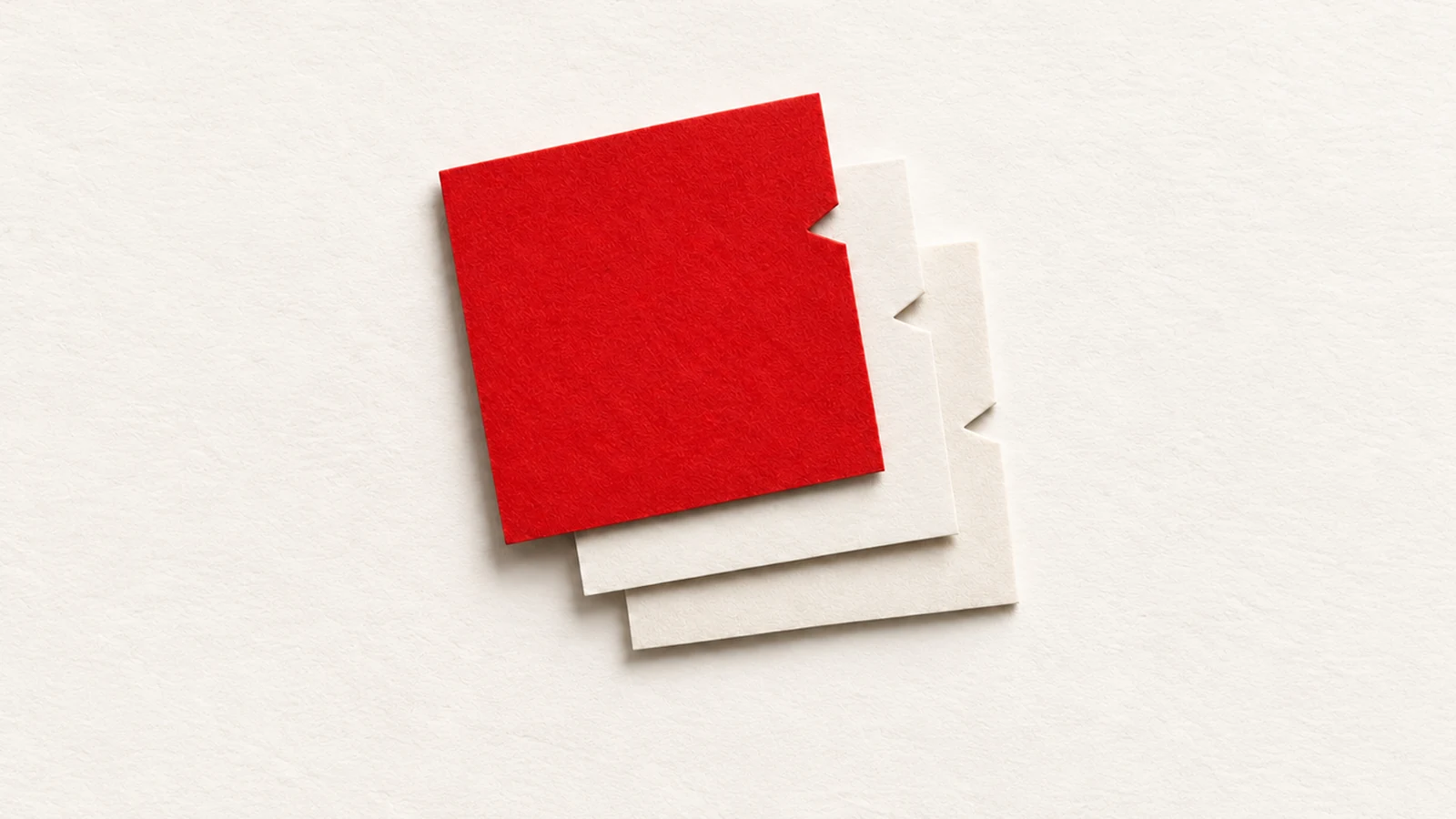 Three overlapping paper sheets, one red and two pale, each have a small angular notch along the exposed right edge.